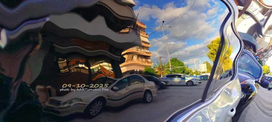 Corrupted reflection of parked cars and buildings in a curved mirror, capturing a sunny street scene.