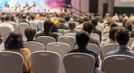 People attending a conference or presentation in an indoor theater setting.